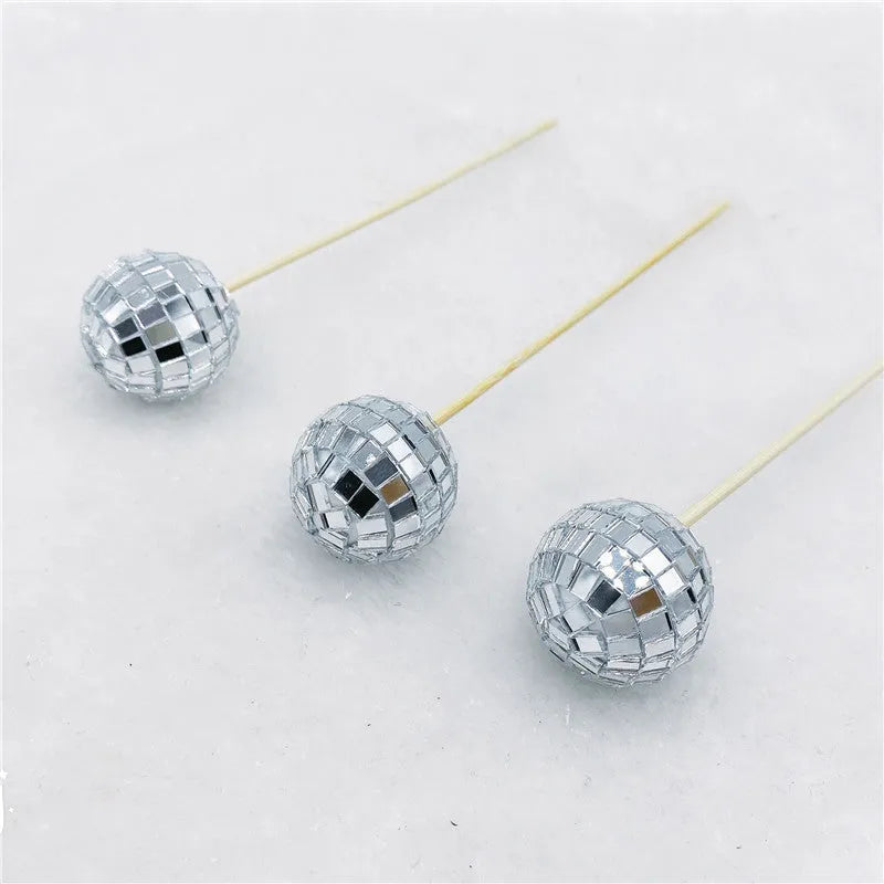 Silver reflective glass disco ball cake topper on a wooden stick for birthday party decoration.