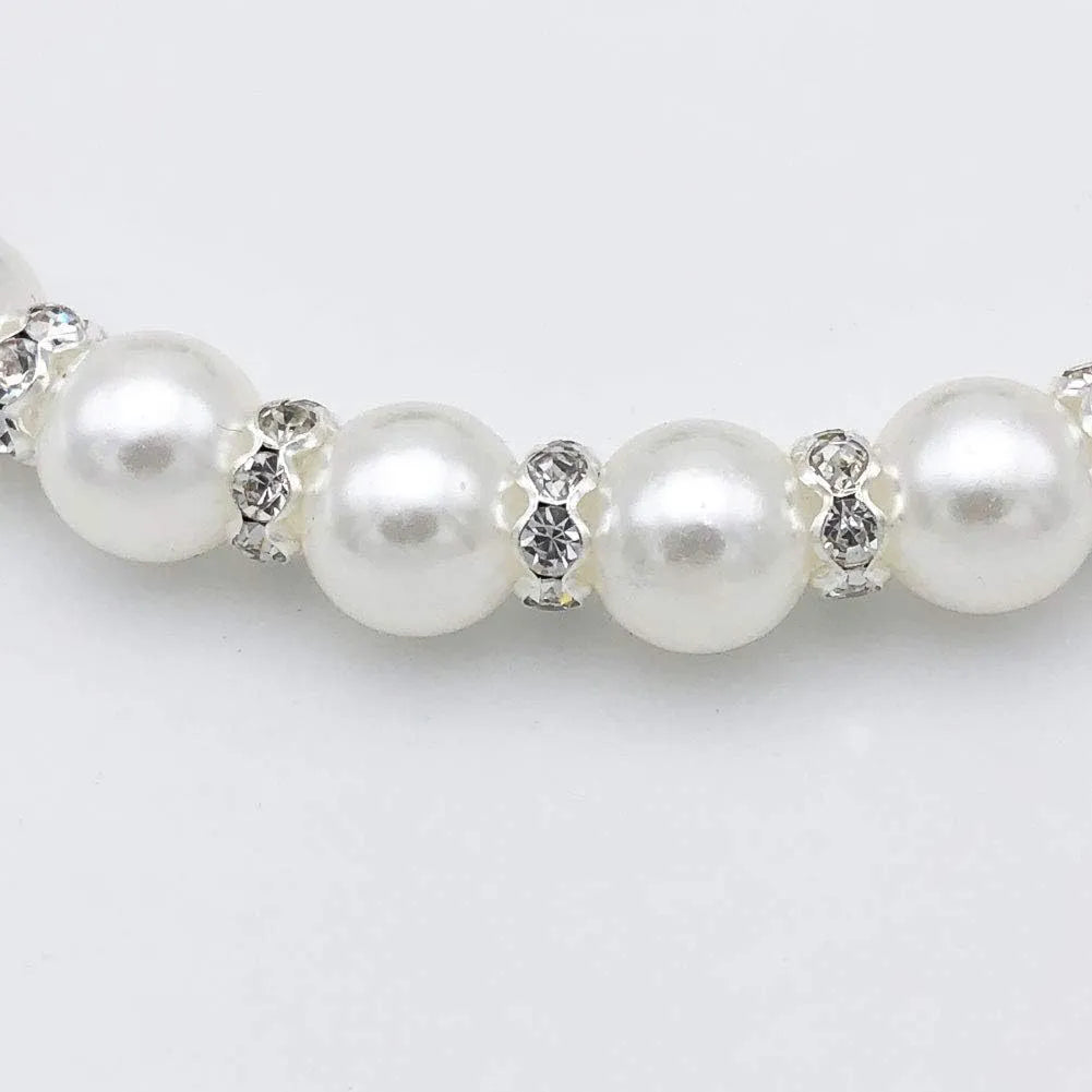 Small dog wearing a blue adjustable pearl and rhinestone necklace with a ribbon bow.