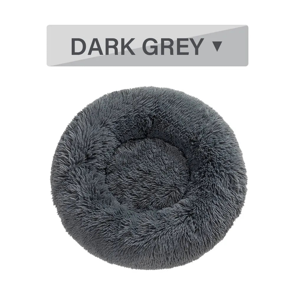 Fluffy donut-shaped dog bed in long plush material, shown in a light grey colour with a raised edge.