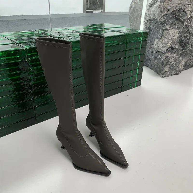 Black pointed toe below knee boots with stiletto heel and back zipper on woman's leg