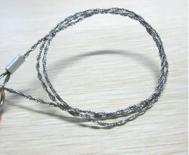 Close-up of a coiled stainless steel survival wire saw with metal pull rings on a wooden background.