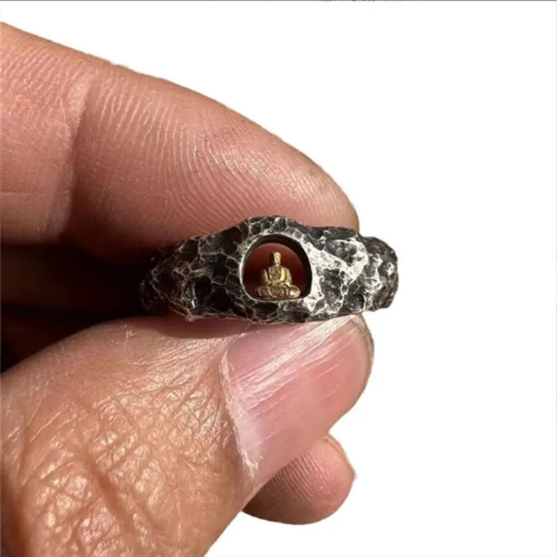 Close-up of a hand-forged copper ring with a rough rock texture and a detailed Buddha motif, shown on a finger.