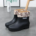 Women's mid-calf PVC rain boot in black on a wet surface.