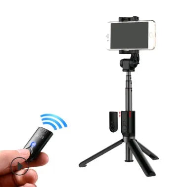 Black Bluetooth selfie stick with extended tripod legs and remote control next to a mobile phone.