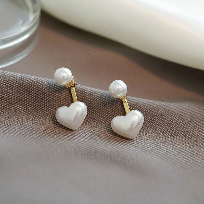 Korean style women's heart shaped stud earrings with pearl-like artificial gemstone inlay on a white background.