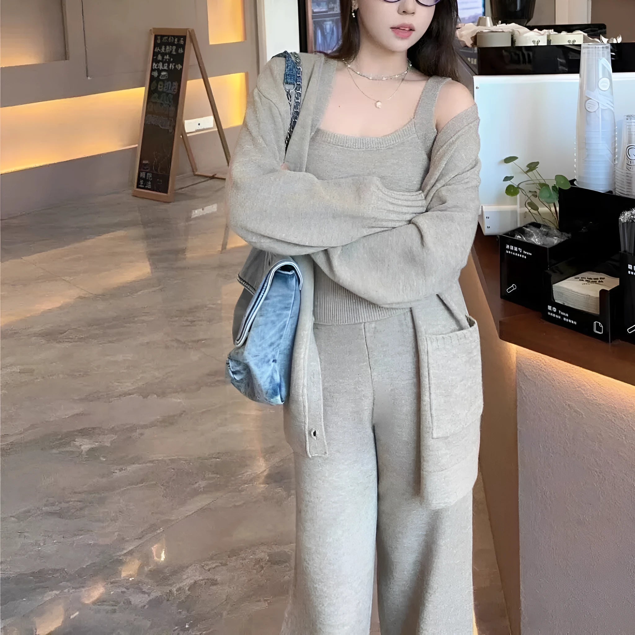 Women's beige knitted cardigan three-piece set with sleeveless vest and suspender trousers on a hanger.