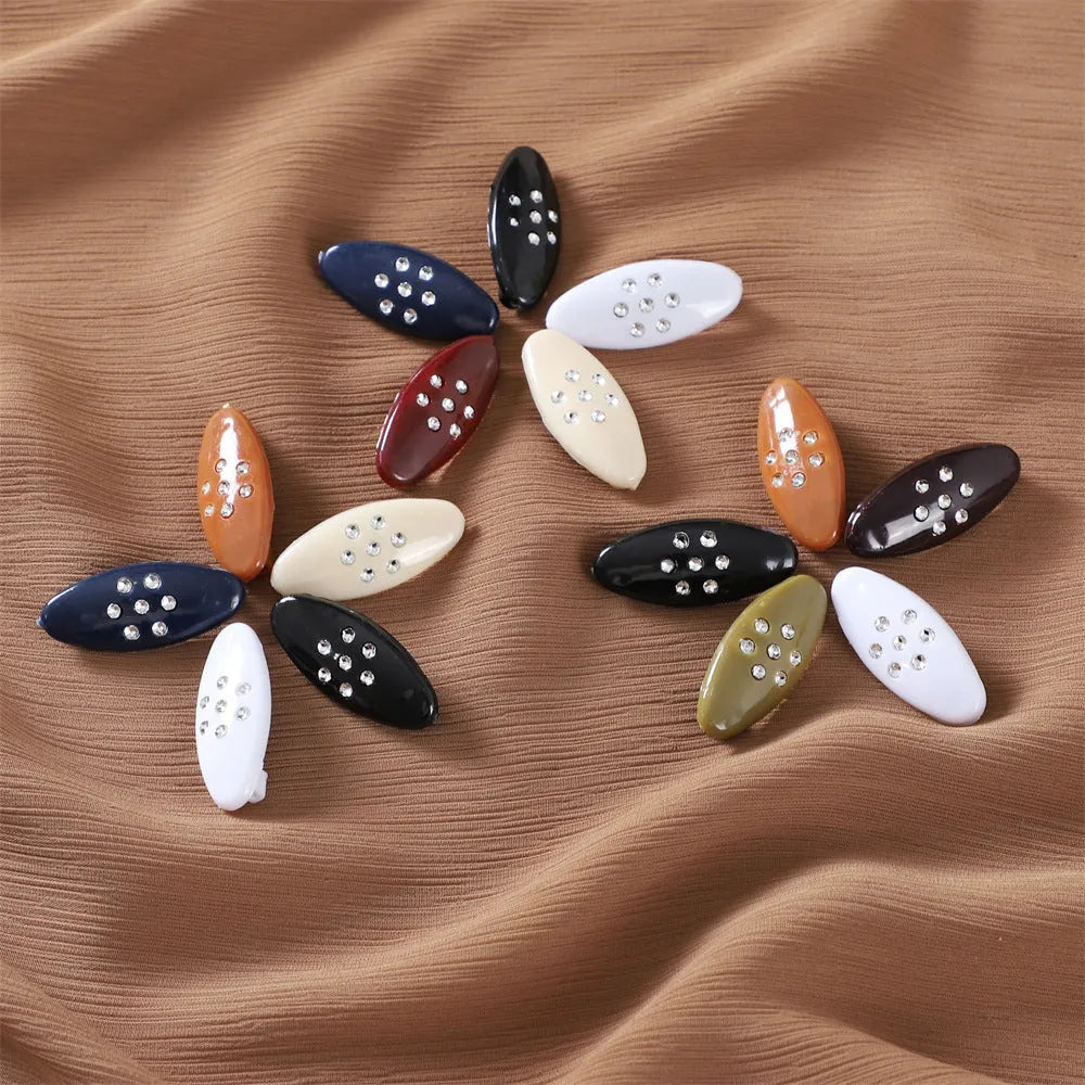 Three plastic plum blossom shaped safety pin brooches with imitation diamond finish on a light background
