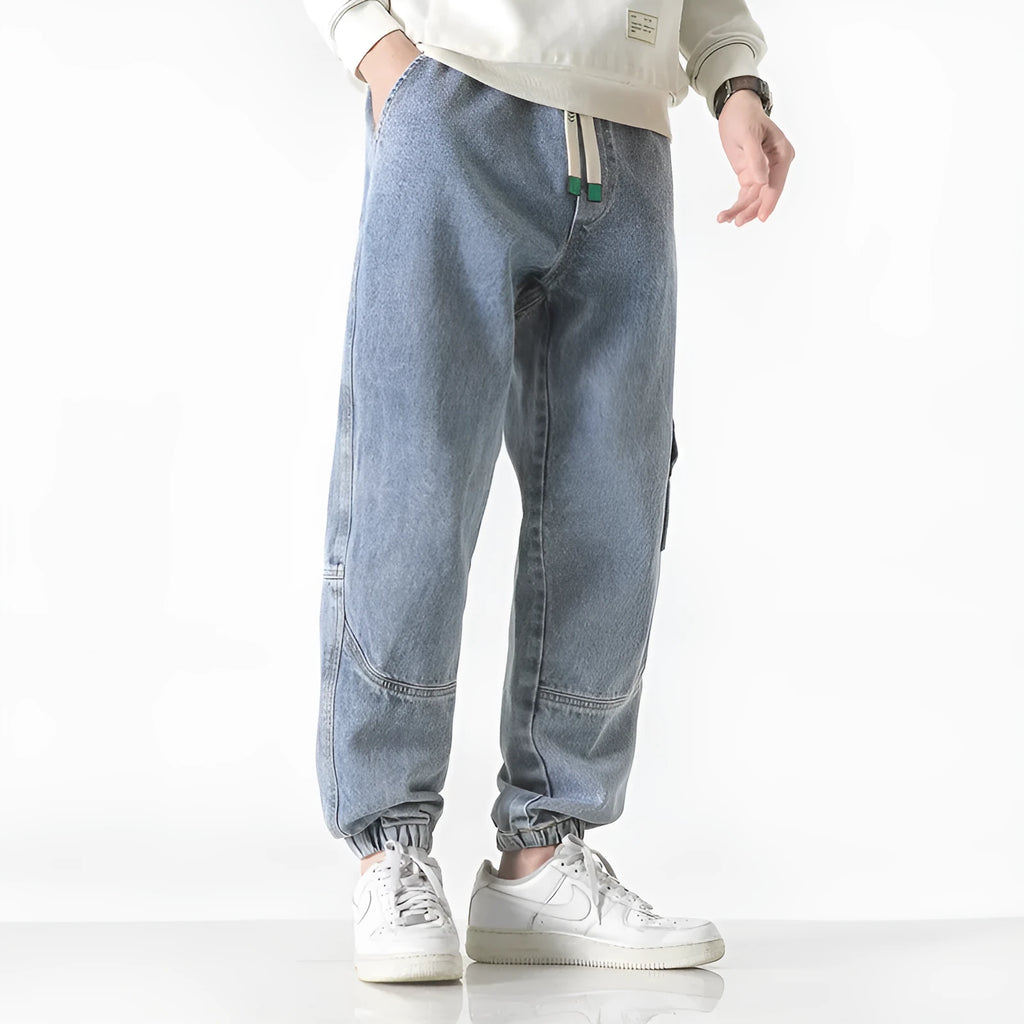 Men's black loose-fit tapered cotton trousers on a hanger, showing the mid-waist and tapered leg design.