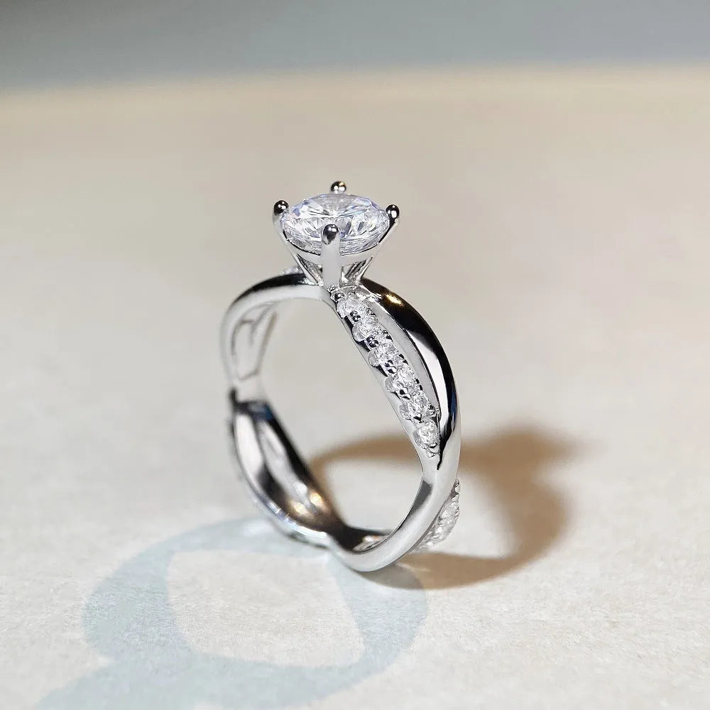 Silver geometric cross ring with a 1 karat moissanite stone in a four-claw setting on a twisted band.