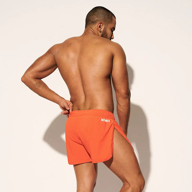 Men's loose orange beach shorts with elastic waistband on a sandy shore