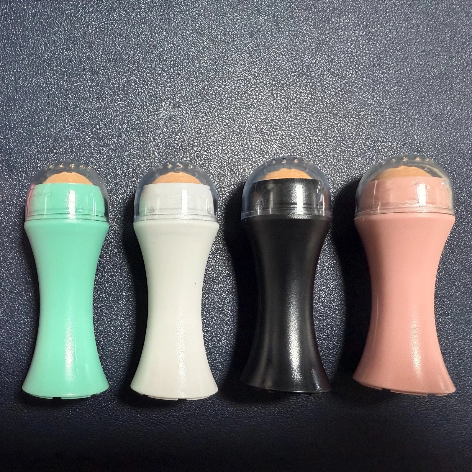 Volcanic stone facial roller for oily skin control in black, green, pink, or white colours.
