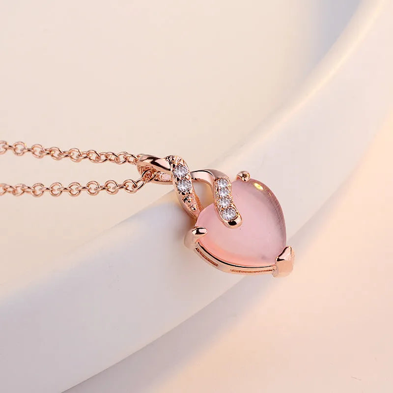 Rose gold cross chain necklace with a pink heart-shaped synthetic crystal pendant.