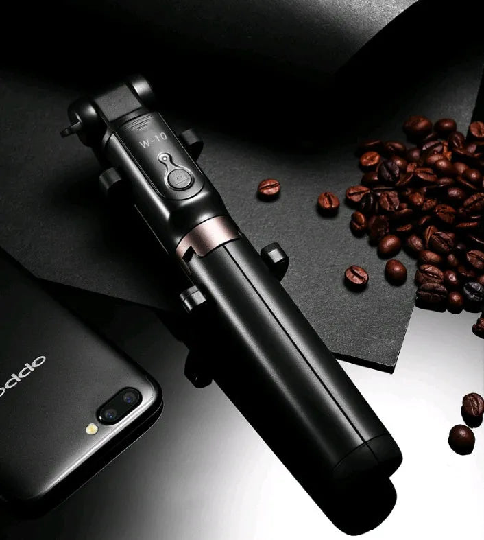 Black Bluetooth selfie stick with extended tripod legs and remote control next to a mobile phone.
