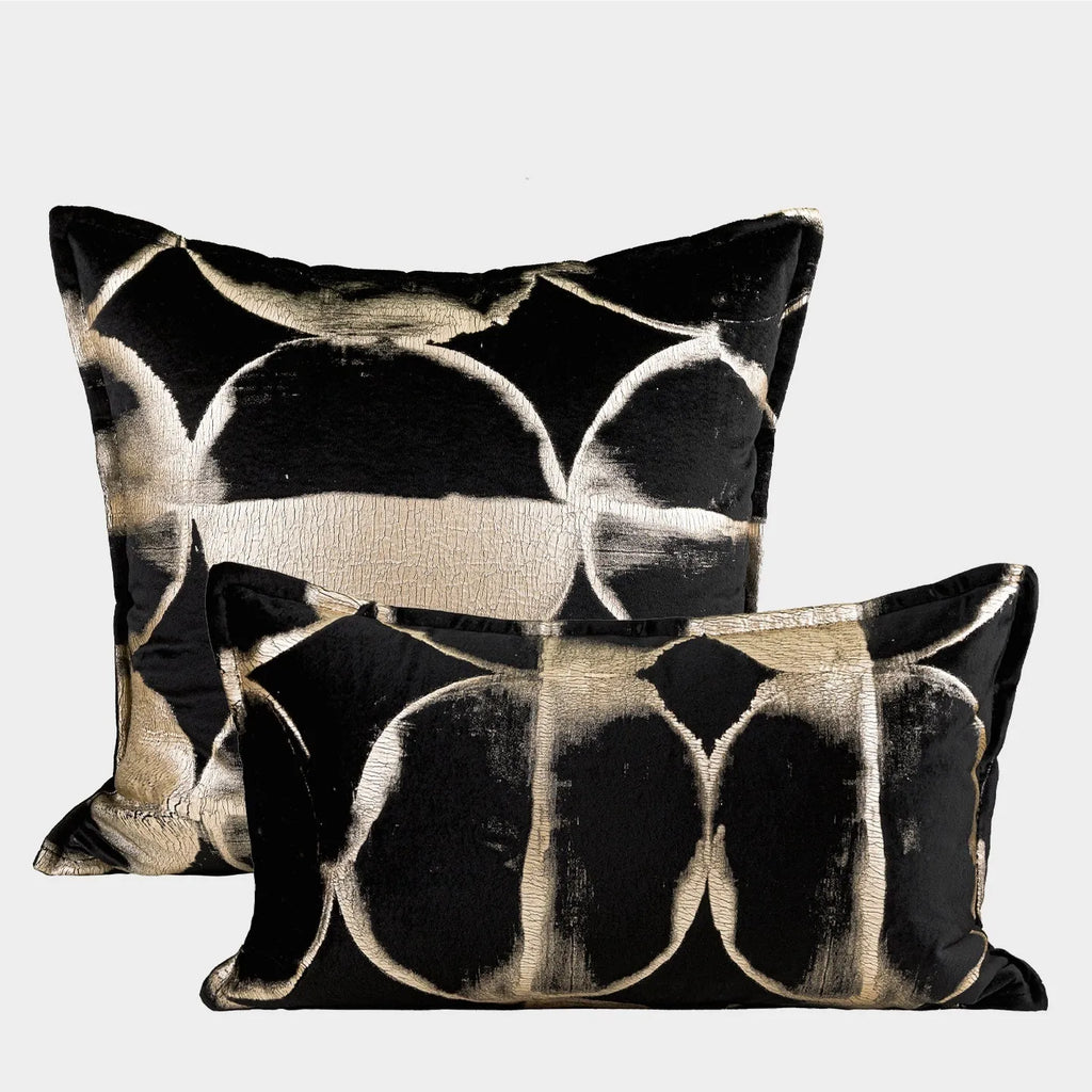 Black and gold abstract patterned flannel decorative pillow with removable cover on a grey sofa.