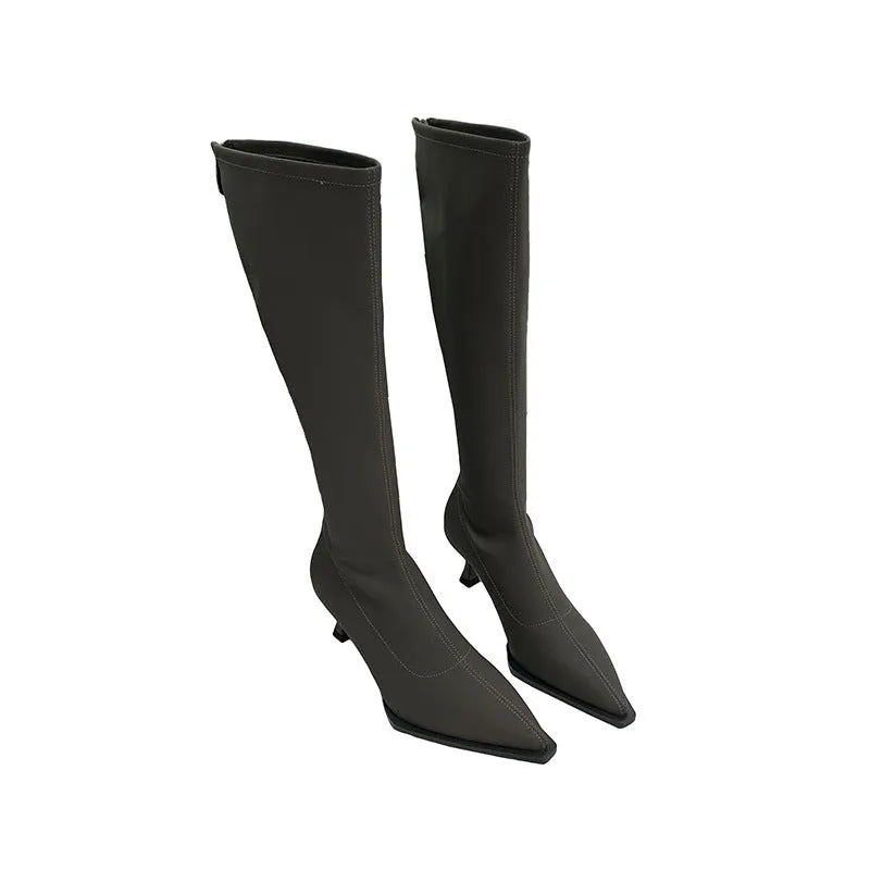 Black pointed toe below knee boots with stiletto heel and back zipper on woman's leg