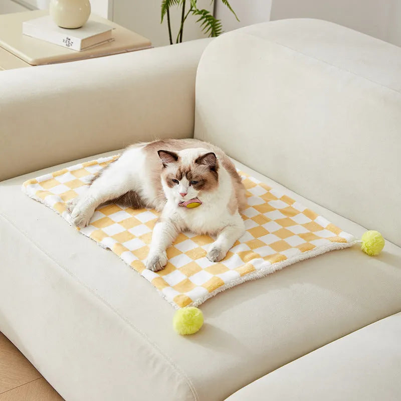 Green plaid pattern pet blanket with fur ball decoration on a sofa.