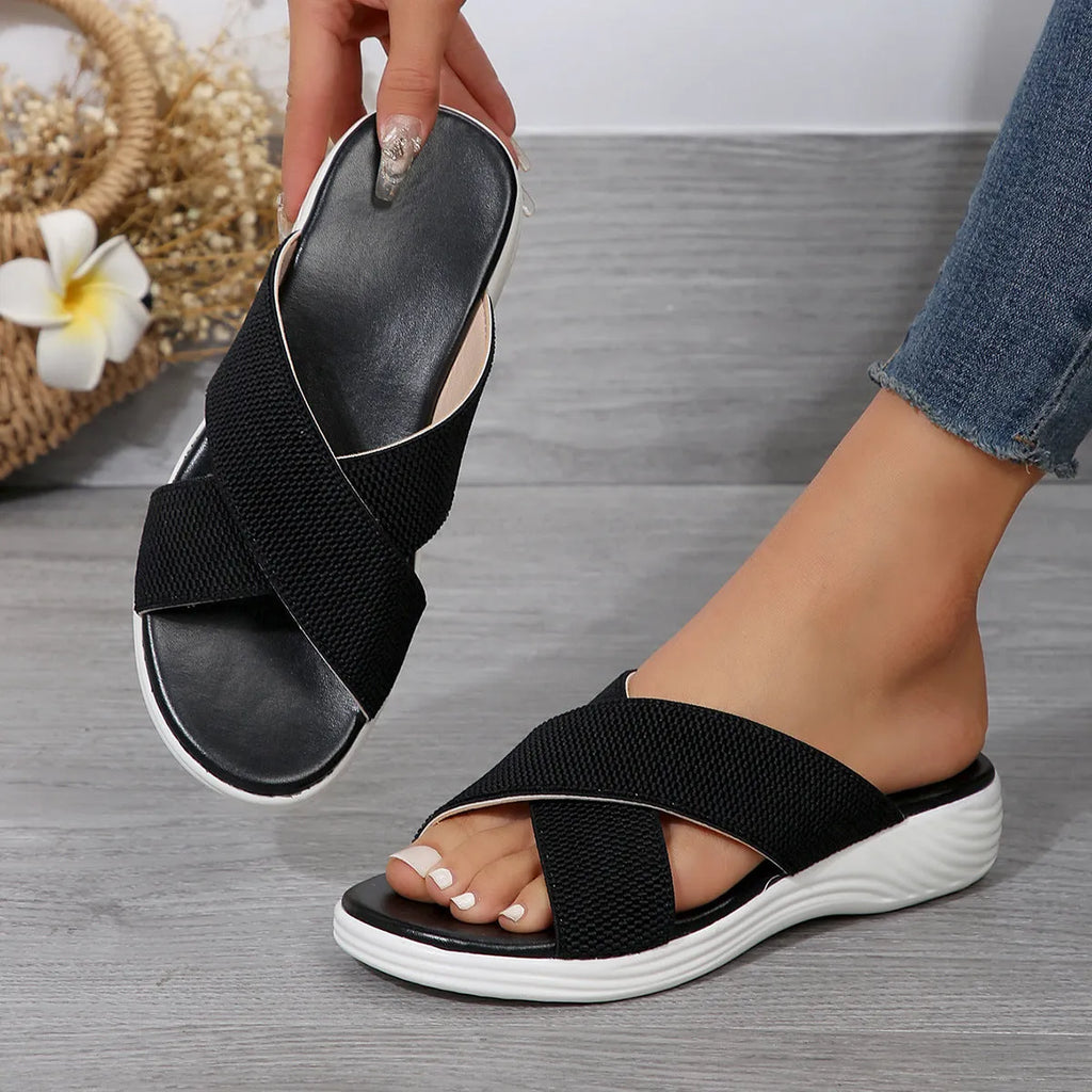 Black women's peep-toe wedge slippers with a thick rubber sole on a plain background.