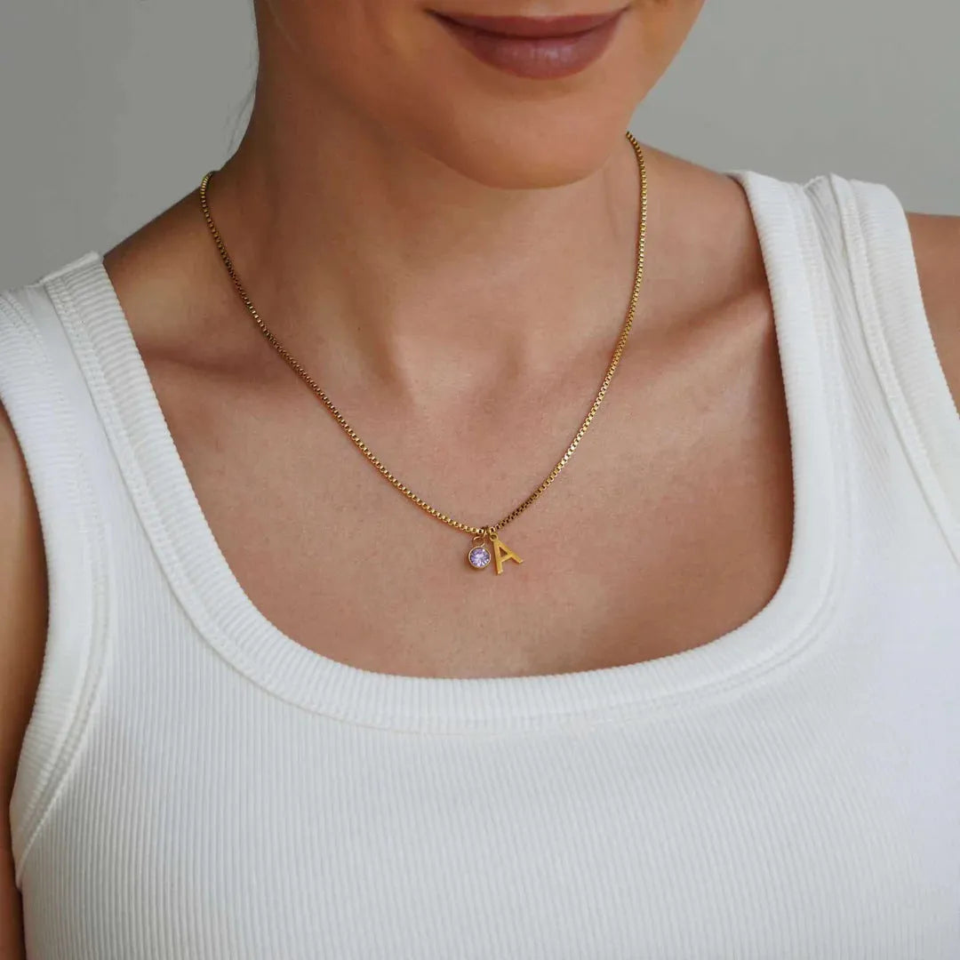 Gold coloured titanium steel birthstone initial pendant necklace with O-ring chain on white background