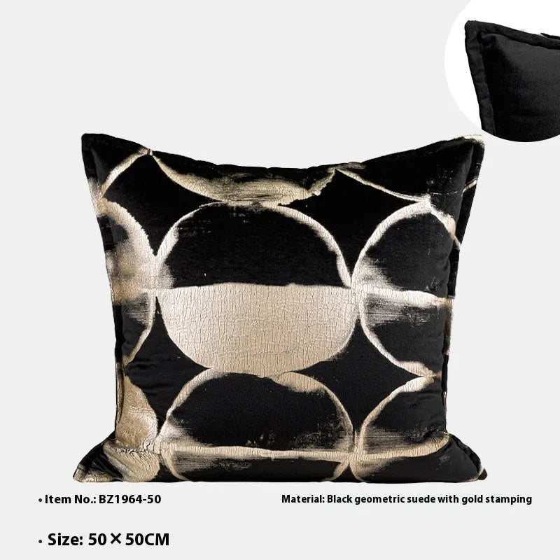 Black and gold abstract patterned flannel decorative pillow with removable cover on a grey sofa.