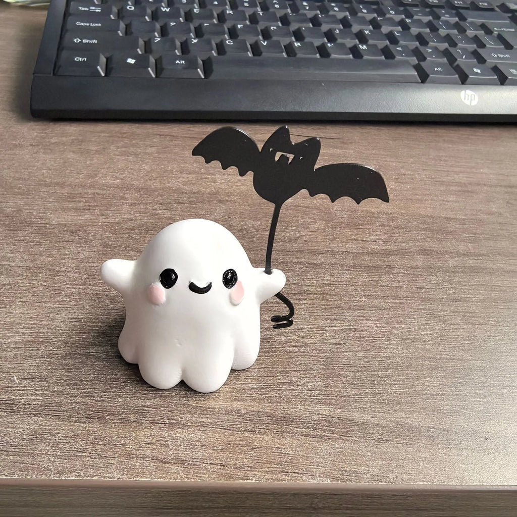 Miniature resin statue of a ghost walking a dog that is holding a bat, a Halloween decoration.