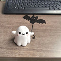 Miniature resin statue of a ghost walking a dog that is holding a bat, a Halloween decoration.