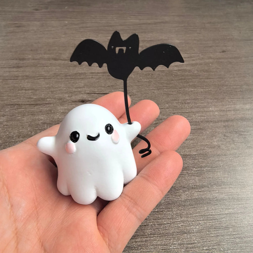 Miniature resin statue of a ghost walking a dog that is holding a bat, a Halloween decoration.