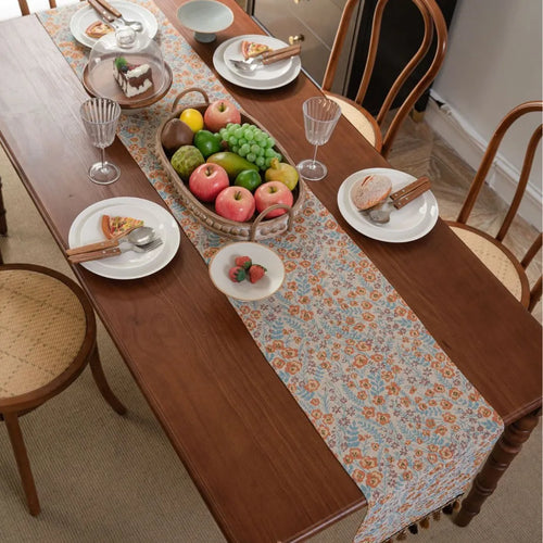 Beige jacquard table runner with floral pattern and long tassels laid flat on a table.