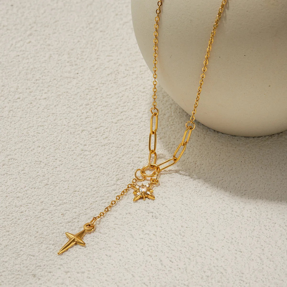 Close up of an 18K gold finish stainless steel necklace with white diamond eight-pointed stars pendant on a regular chain