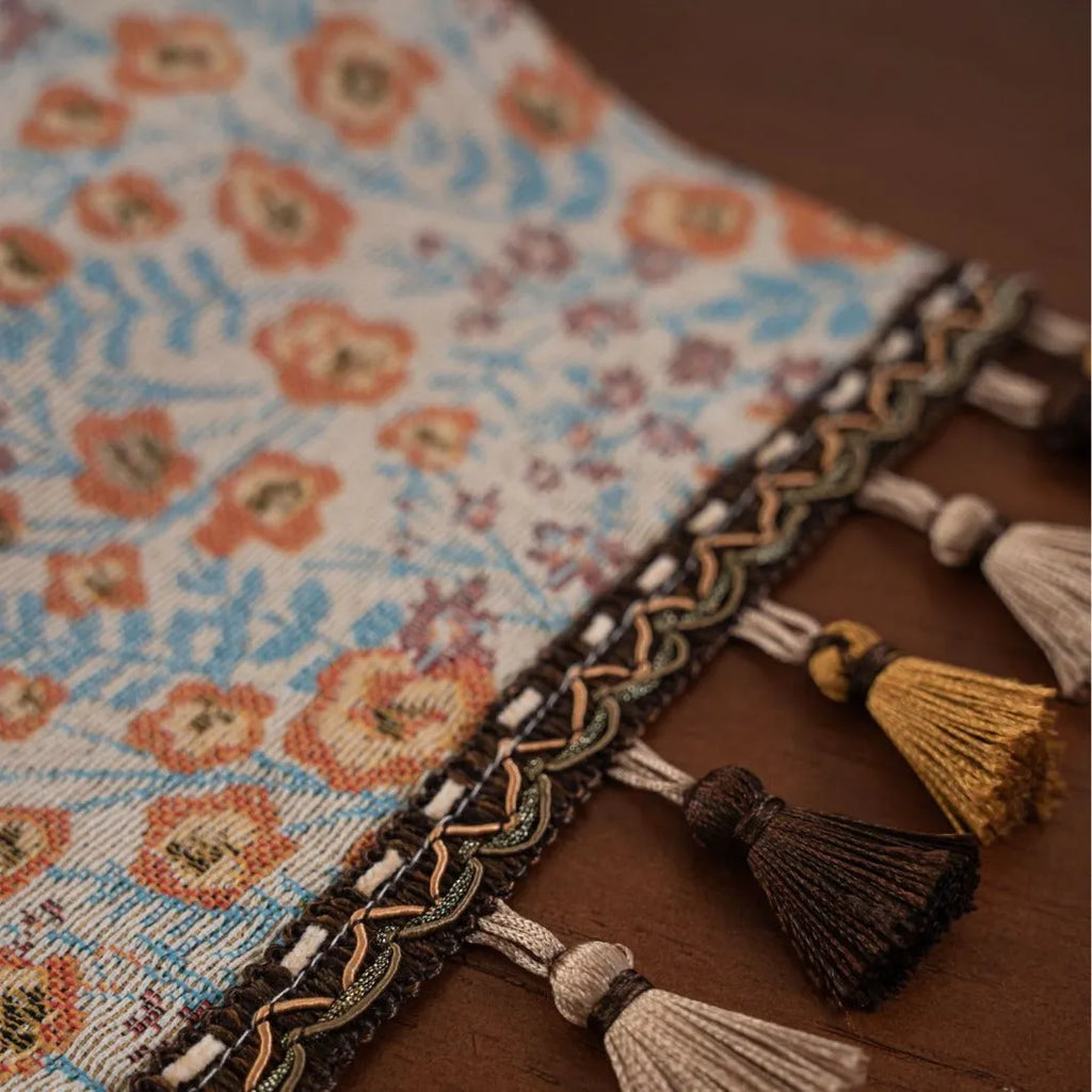 Beige jacquard table runner with floral pattern and long tassels laid flat on a table.