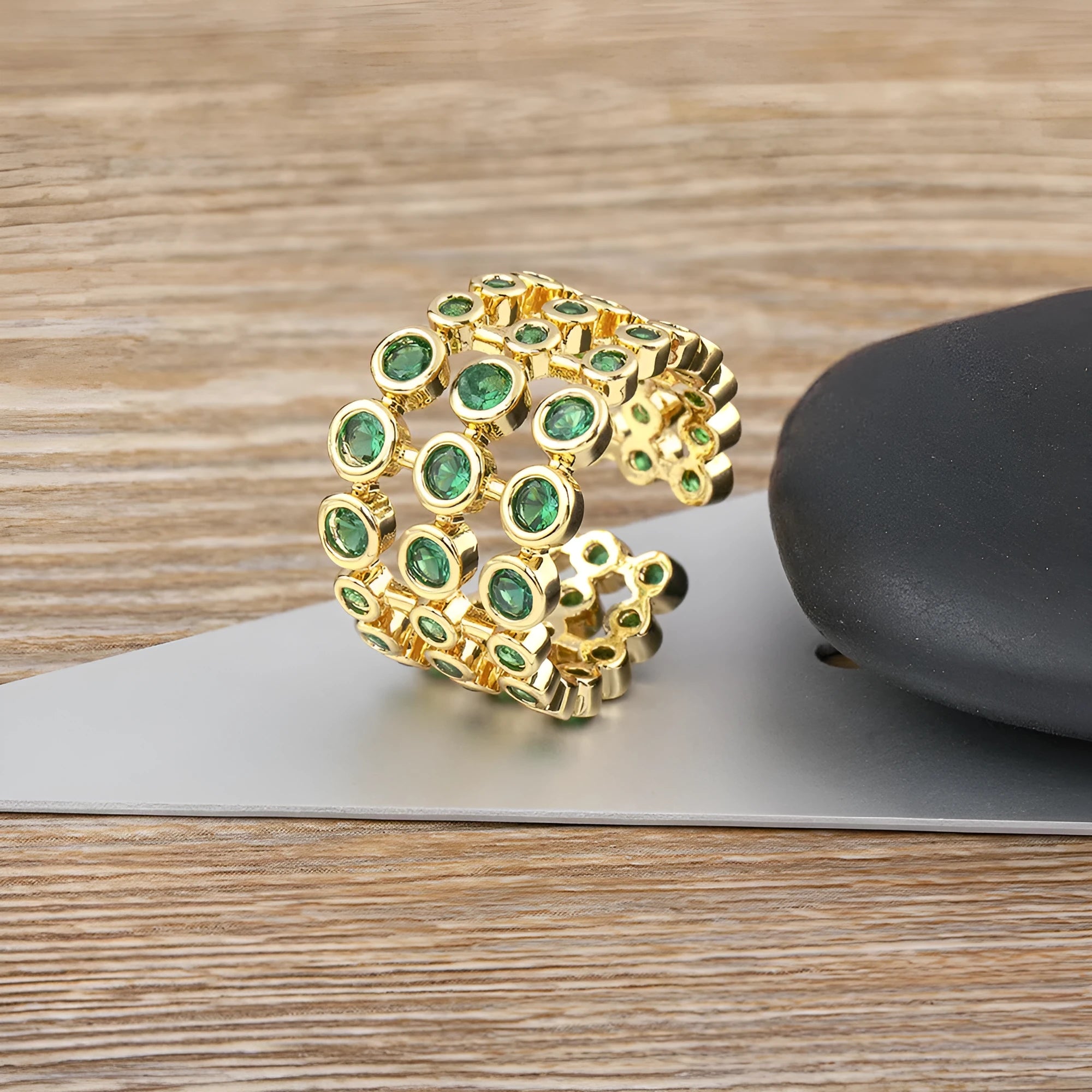A wide, gold-coloured ring with a three-layer design and a large green cubic zirconia stone on a copper base.