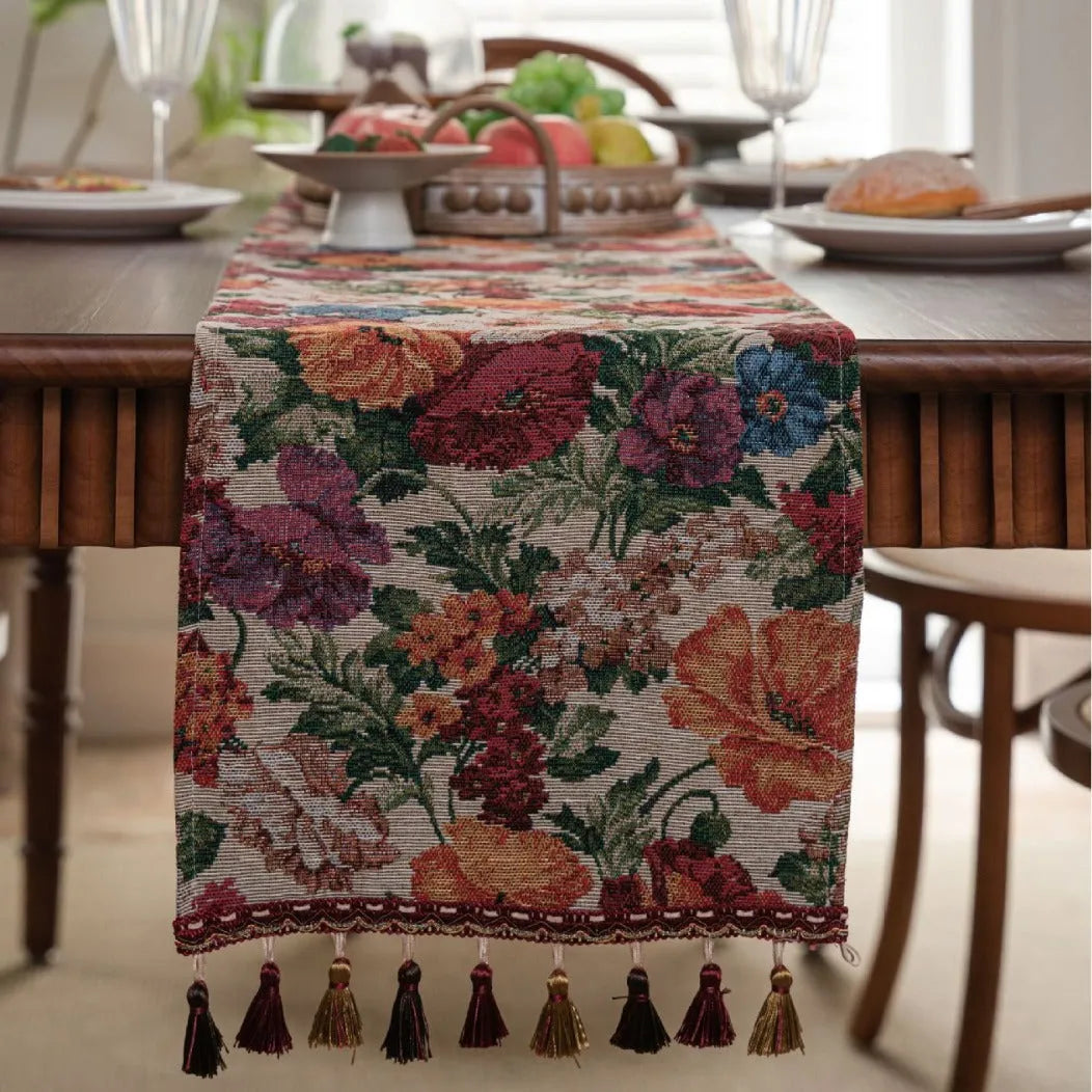 Beige jacquard table runner with floral pattern and long tassels laid flat on a table.