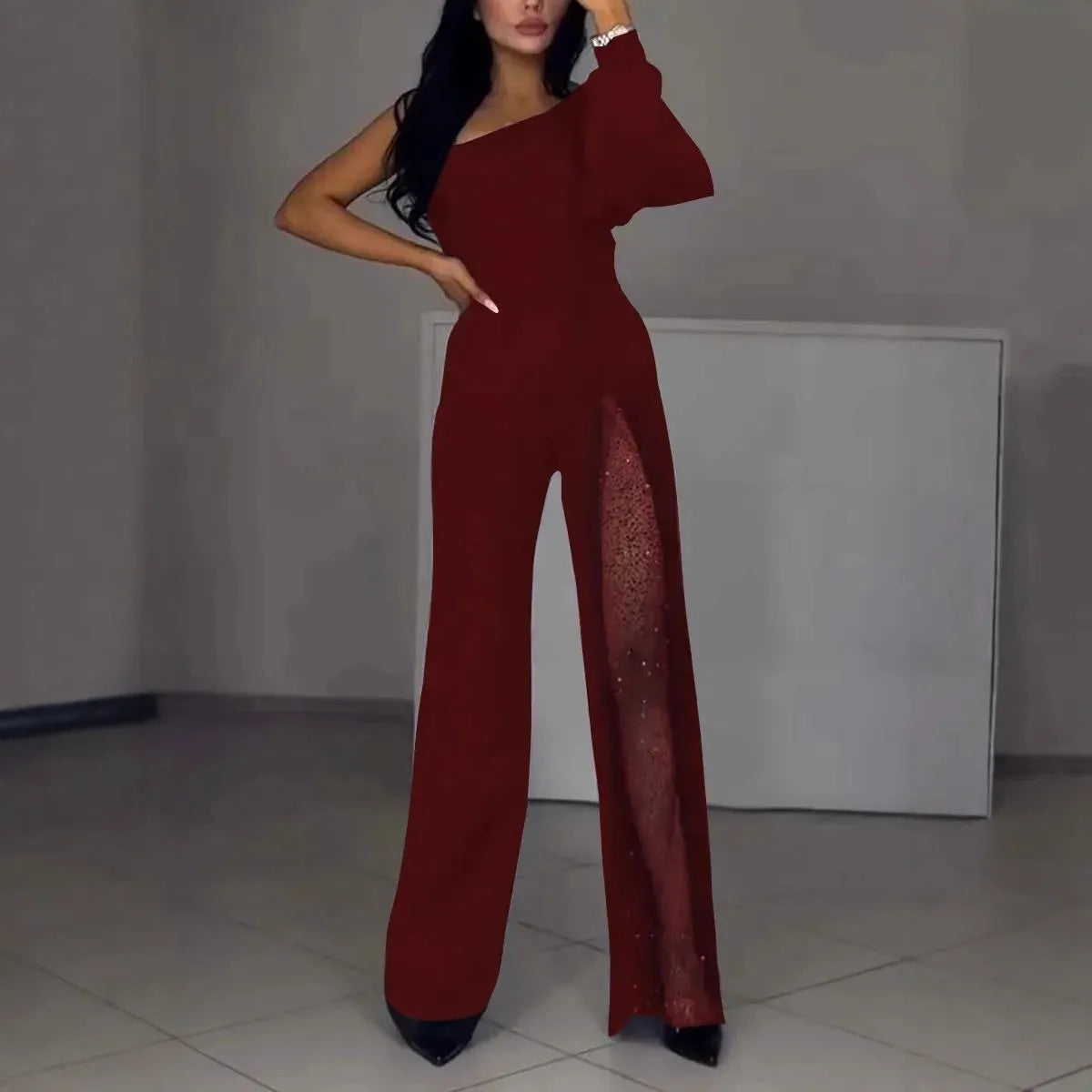 A woman wearing a black oblique shoulder jumpsuit with a high leg slit, made of polyester.