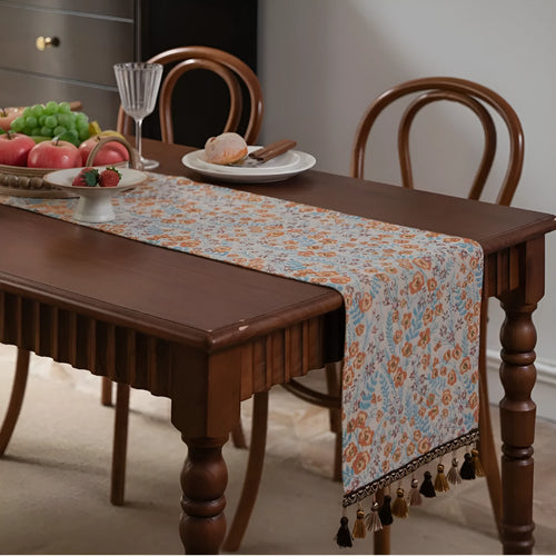Beige jacquard table runner with floral pattern and long tassels laid flat on a table.