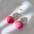 A pair of women's earrings with a clear acrylic peach charm on copper posts