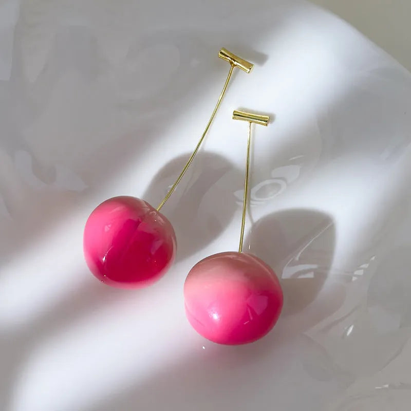 A pair of women's earrings with a clear acrylic peach charm on copper posts