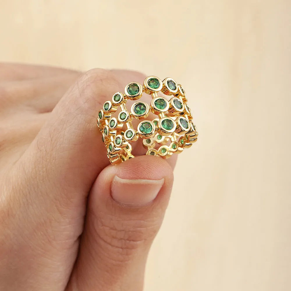 A wide, gold-coloured ring with a three-layer design and a large green cubic zirconia stone on a copper base.