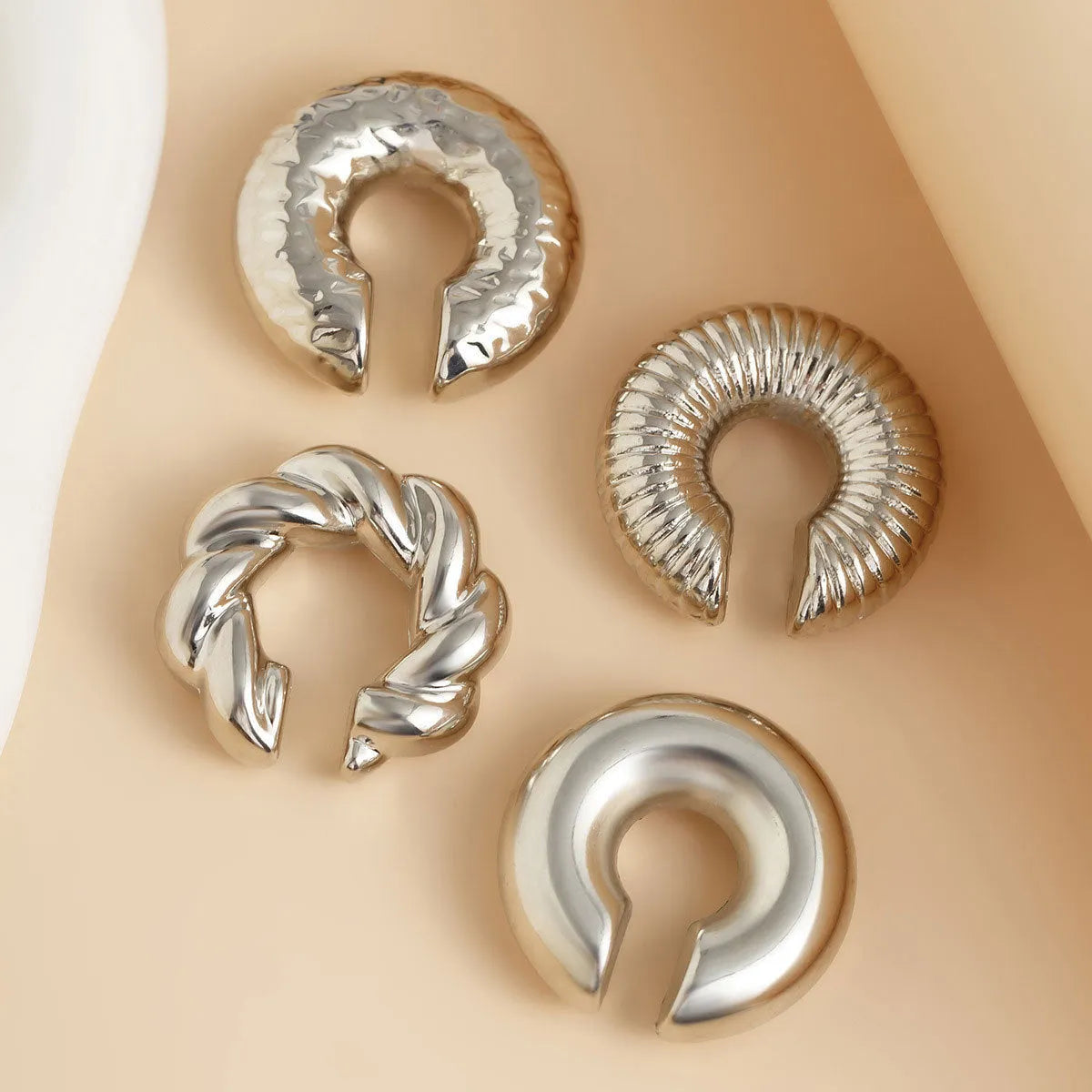 Set of four geometric clip-on earrings for women in gold or silver colour on a white background.