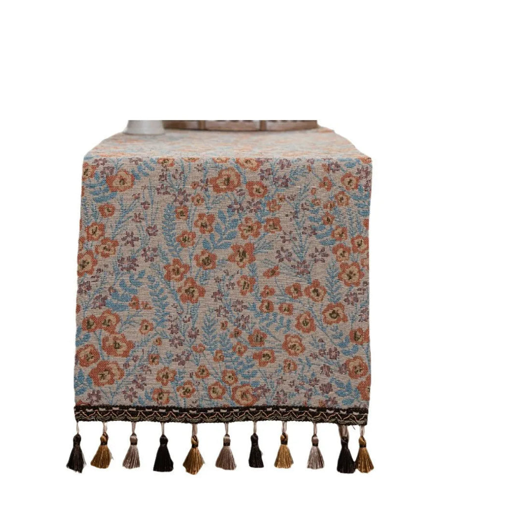 Beige jacquard table runner with floral pattern and long tassels laid flat on a table.