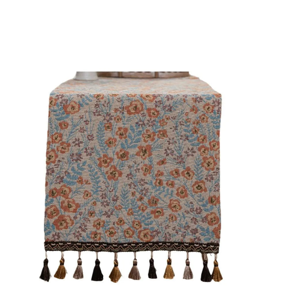 Beige jacquard table runner with floral pattern and long tassels laid flat on a table.