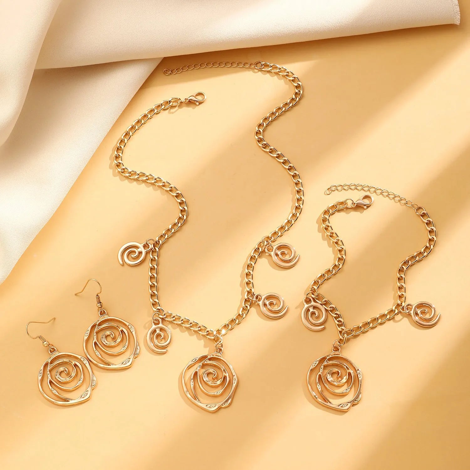 Women's spiral donut jewellery set showing matching necklace, bracelet and ear hooks in gold or silver electroplated alloy