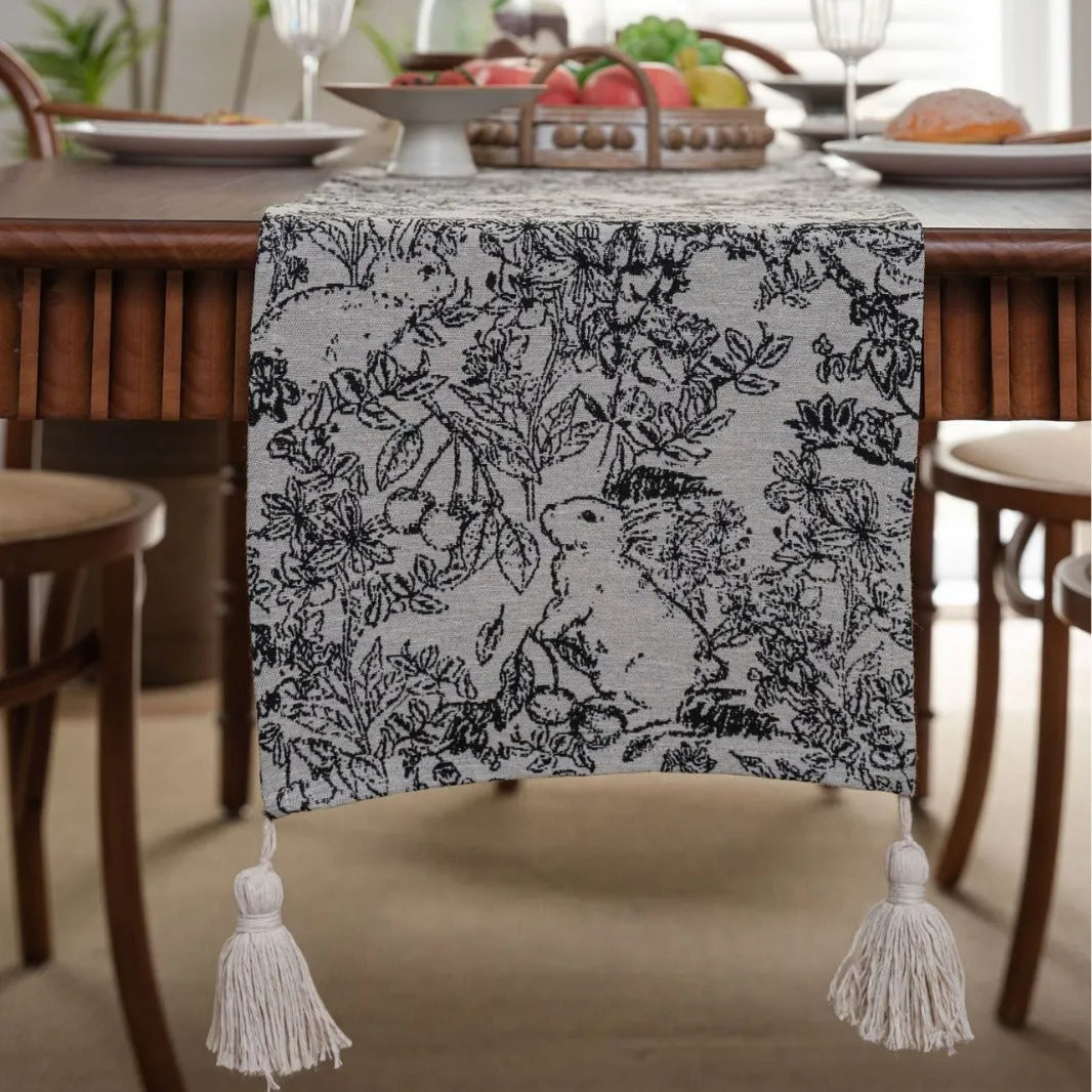Beige jacquard table runner with floral pattern and long tassels laid flat on a table.