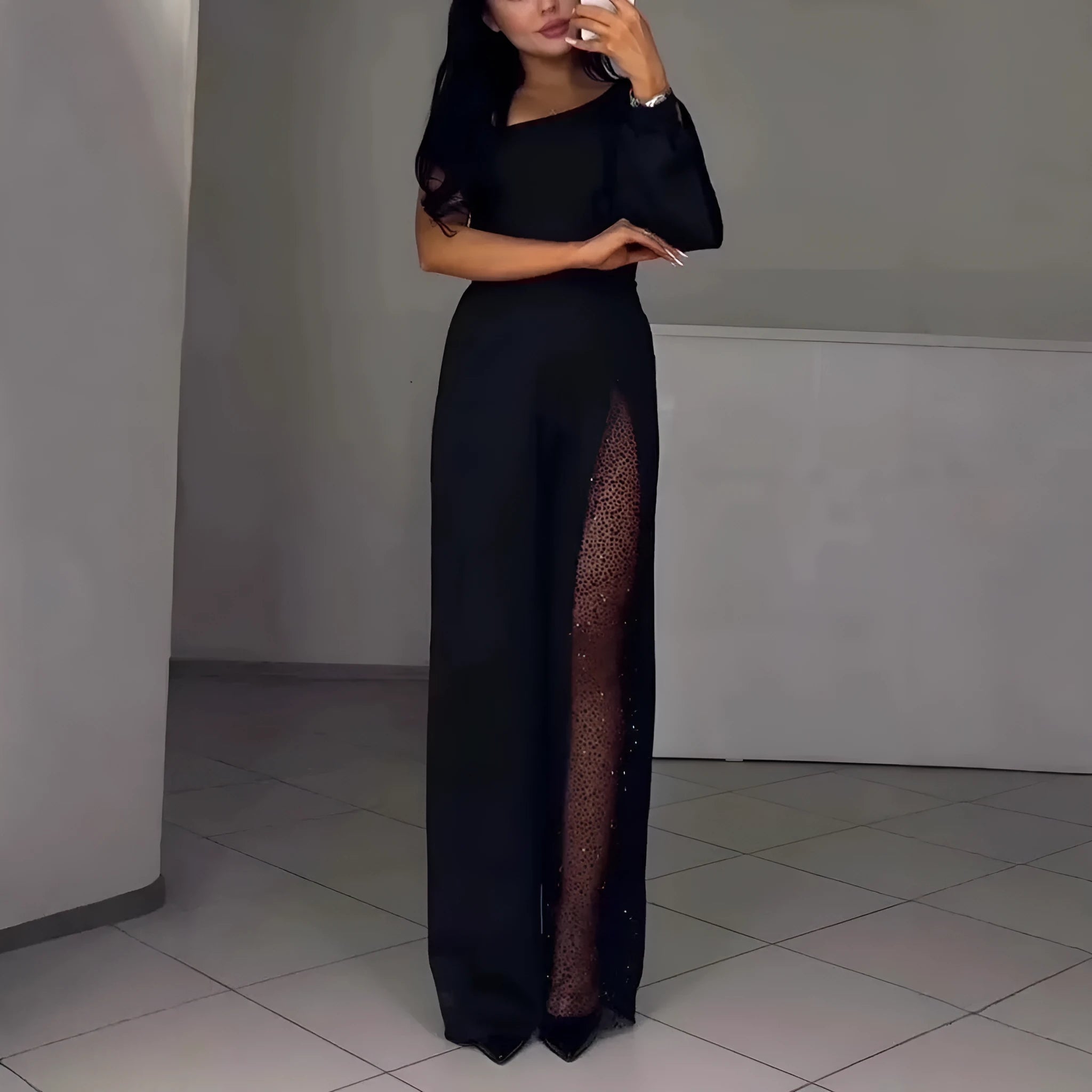A woman wearing a black oblique shoulder jumpsuit with a high leg slit, made of polyester.