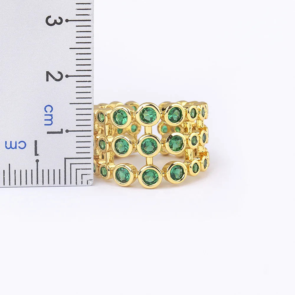 A wide, gold-coloured ring with a three-layer design and a large green cubic zirconia stone on a copper base.