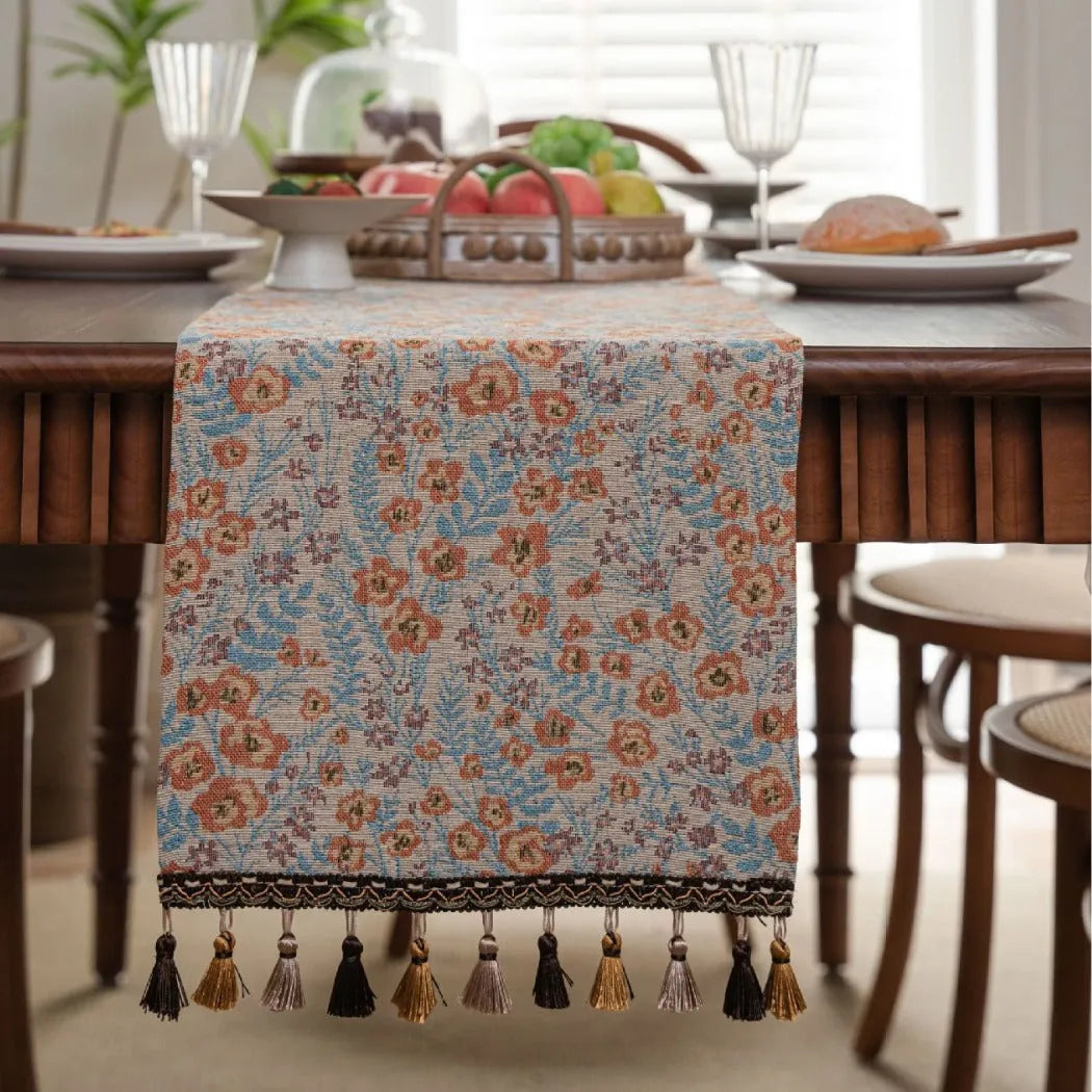 Beige jacquard table runner with floral pattern and long tassels laid flat on a table.