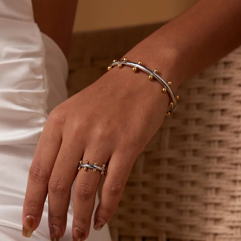 Stainless steel C-shaped bean bead with textured rivet detail in gold, silver, and two-tone finishes.