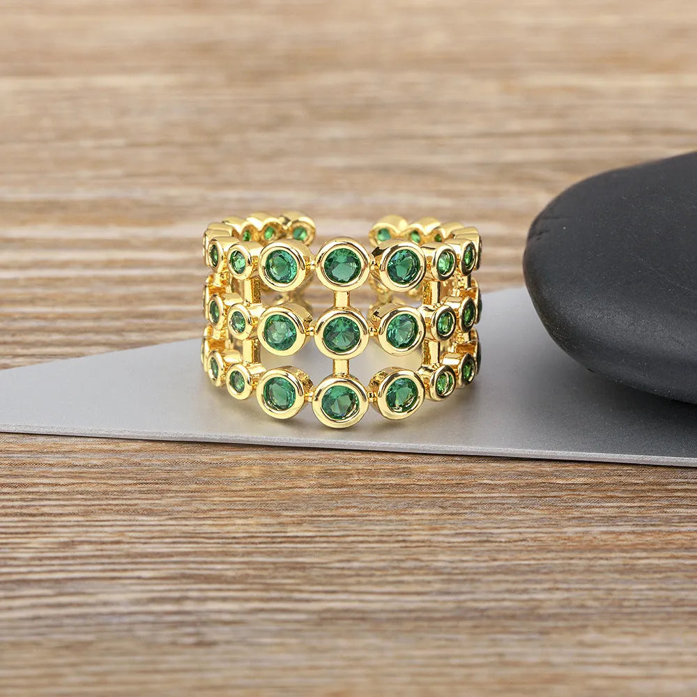 A wide, gold-coloured ring with a three-layer design and a large green cubic zirconia stone on a copper base.