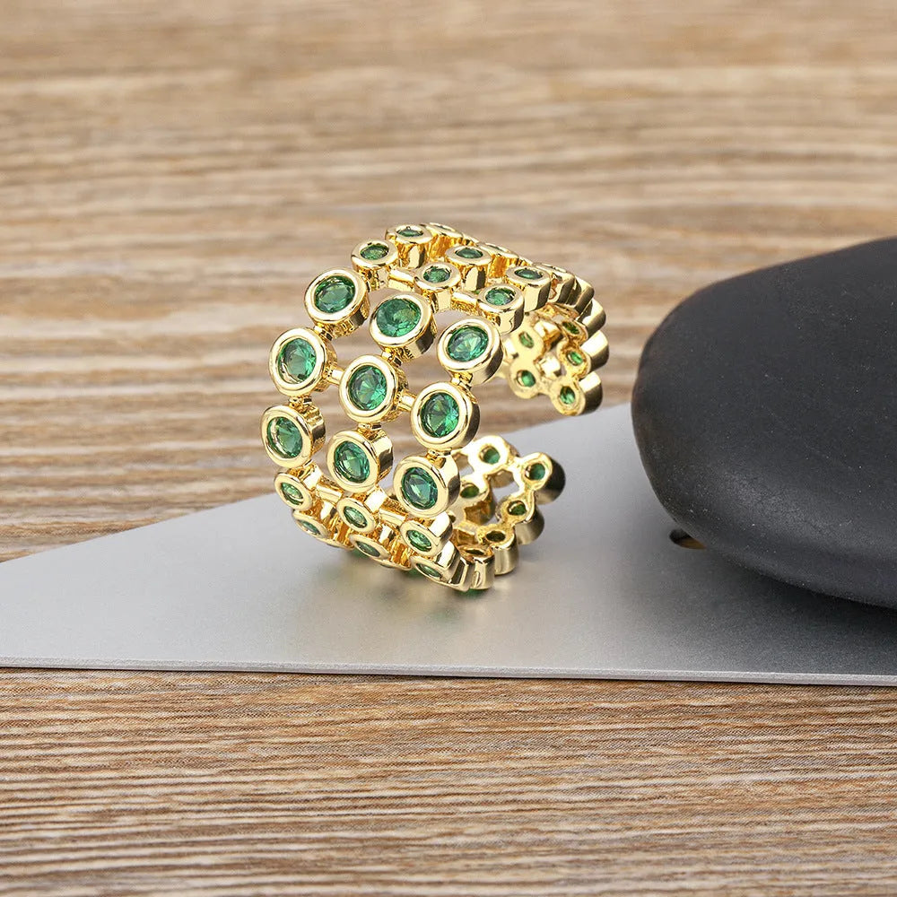 A wide, gold-coloured ring with a three-layer design and a large green cubic zirconia stone on a copper base.