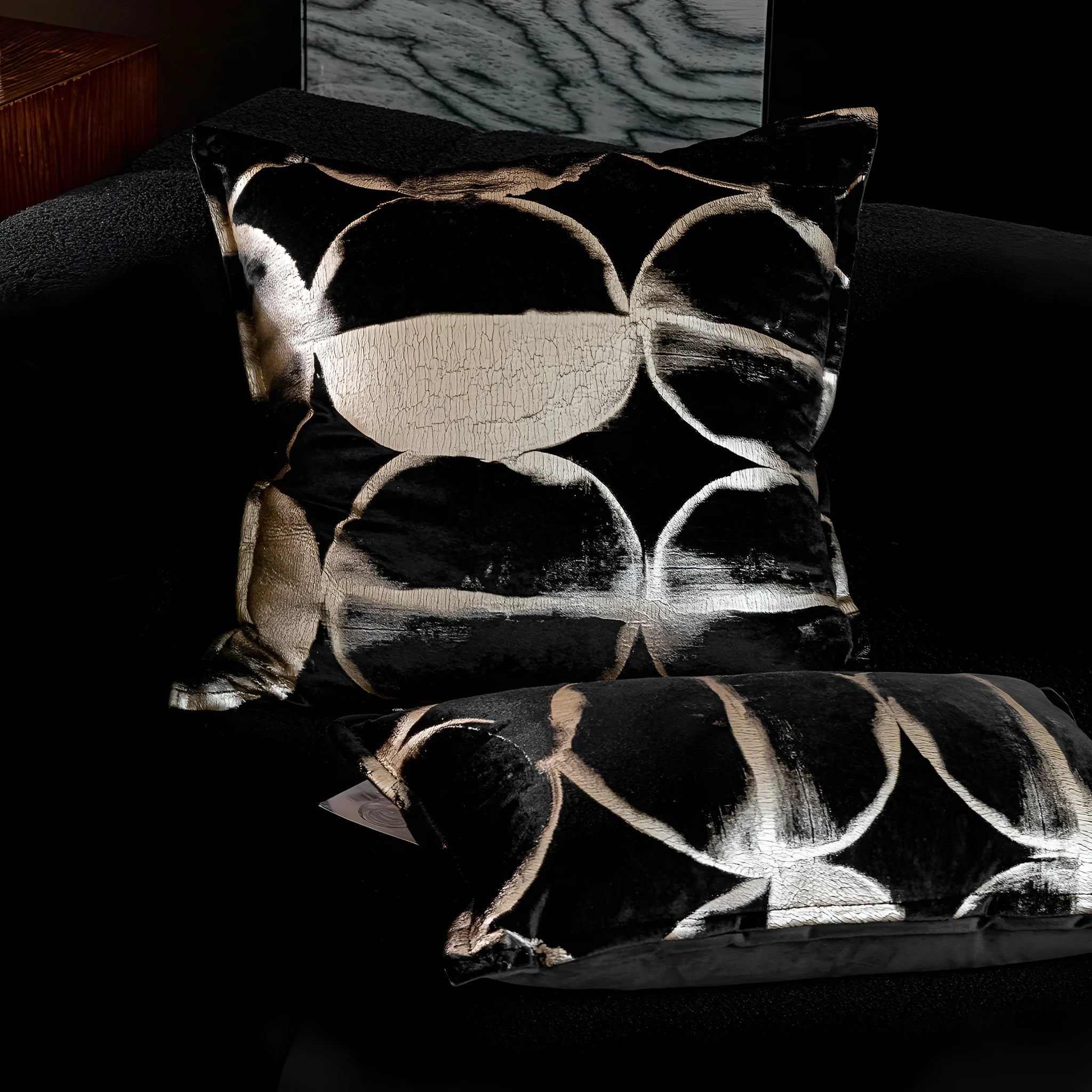 Black and gold abstract patterned flannel decorative pillow with removable cover on a grey sofa.