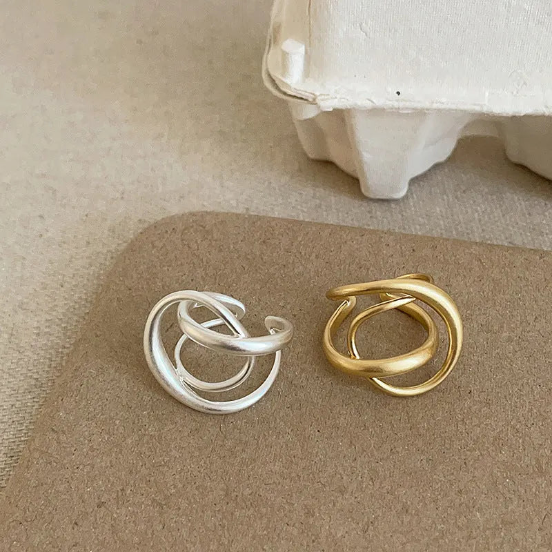 Matte metal open ring with three-dimensional interlaced geometric design in gold or silver finish.