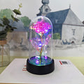Small glass cover night lamp with plastic flowers on a black base, showing coloured light illumination.